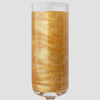 A clear champagne flute filled with golden FND TESTING - 24k Magic Edible Glitter by Jenna Rae Cakes shimmers against a plain light gray background.