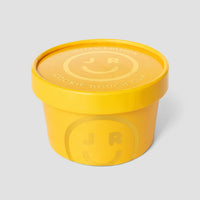 A yellow Cookie Dough Cup with a matching lid features the Jenna Rae Cakes name and a smiley face logo, displayed against a plain light gray background.