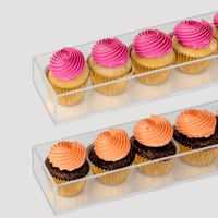 The Dessert Tables by Jenna Rae Cakes features two clear rectangular trays on a light gray background—one with four pink-frosted cupcakes, the other with four orange-frosted cupcakes topped with chocolate sprinkles.