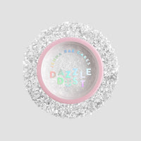 A small round container with a pink rim and clear lid labeled Jenna Rae Cakes Dazzle Dust Best Seller Trio, filled with fine, sparkly white glitter, sits on a light gray background.