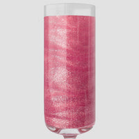 A clear champagne flute holds a vibrant pink drink sparkling with Jenna Rae Cakes Lollipop Edible Glitter, packaged in 5g shakers (set of 6), set against a plain light gray background.
