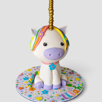 The One-of-a-Kind Cakes by Jenna Rae Cakes features a unicorn cake with a golden horn, rainbow mane, purple accents, and a decorated base with flowers, hearts, and LILIANO in vibrant letters.