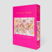 The Sugar Rush Puzzle by Jenna Rae Cakes comes in a bright pink rectangular box featuring a colorful dessert table with pastries, flowers, and sweets, and contains 500 pieces.