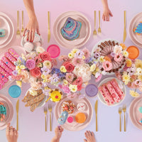 The Sugar Rush Puzzle by Jenna Rae Cakes features a pastel-themed table with colorful pastries, cupcakes, waffles, and donuts amid floral arrangements. Pink, blue, and yellow plates and gold cutlery add to the vibrant celebration scene.