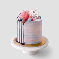 The Half Works Cake by Jenna Rae Cakes is a pastel birthday cake topped with a pink macaron, blue and pink candies, chocolate drizzle, and a white chocolate Happy 17th Birthday disc on a marble stand.