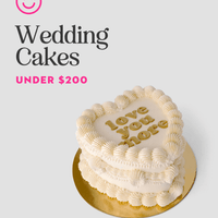 A heart-shaped white wedding cake with “love you more” in yellow icing sits on a gold base. Beside it, text reads “Wedding Cakes Under $200” and a pink and black Jenna Rae Cakes logo appears above.