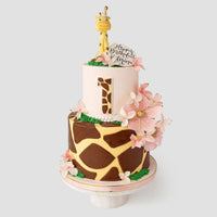 A two-tiered cake with giraffe print patterns, pink flowers, a large number 1, and a giraffe figurine on top, along with a round sign that says Happy Birthday Luna.