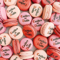A pile of pink and red Printed Macarons by Jenna Rae Cakes, some featuring black lettering on top, are arranged close together to create a colorful and textured pattern.