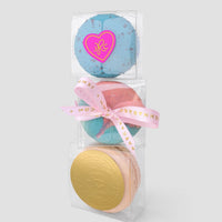 Three stacked Signature Single Macaron Boxes by Jenna Rae Cakes: the top is blue with a heart-shaped sticker, the middle is pink and blue with a pink ribbon, and the bottom is peach with a round gold embossed label.