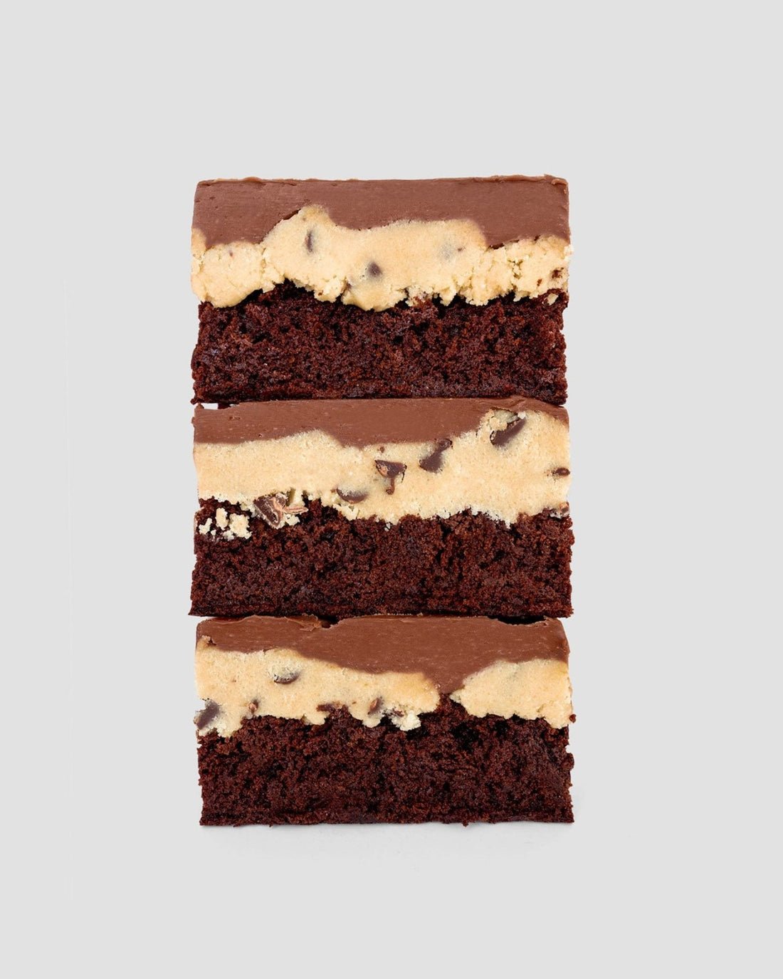Cookie Dough Brownie by Jenna Rae Cakes features three stacked chocolate brownies topped with chocolate chip cookie dough and a chocolate glaze, displayed on a plain light gray background.
