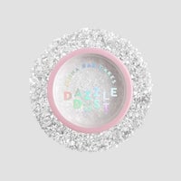 A small round container with a pink rim and clear lid labeled Jenna Rae Cakes Dazzle Dust Best Seller Trio, filled with fine, sparkly white glitter, sits on a light gray background.