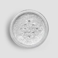 A round container of Jenna Rae Cakes Dazzle Dust Best Seller Trio is filled with fine, shimmery silver glitter powder, shown from above against a light gray background.