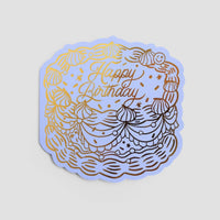 The Jenna Rae Cakes Happy Birthday Greeting Card features a cake illustration with swirls, stars, and a smiley face, topped with “Happy Birthday” in cursive gold foil.