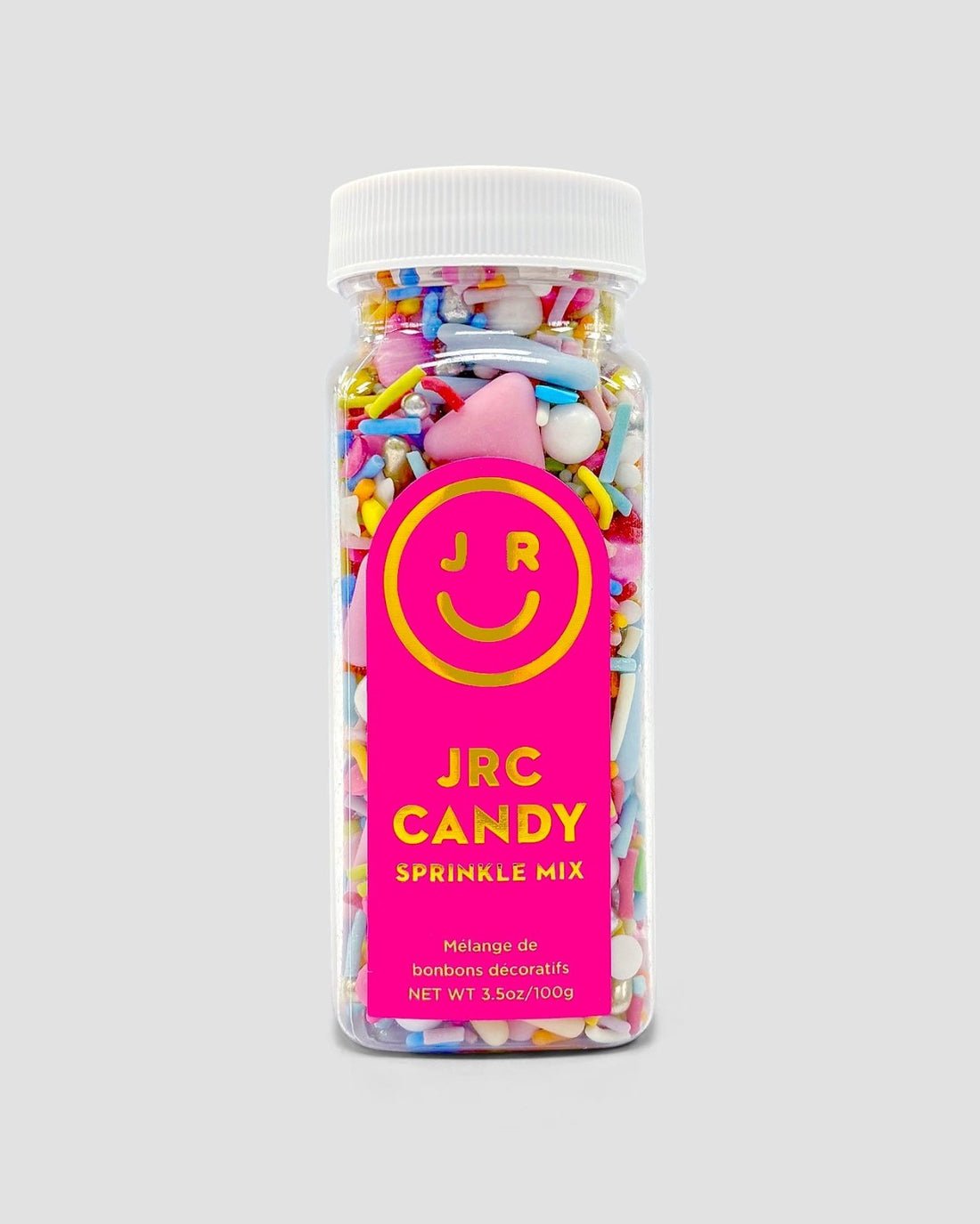 A clear plastic bottle filled with colorful candy sprinkles, featuring a bright pink label with a yellow smiley face and the text Home Baker Bundle by Jenna Rae Cakes.