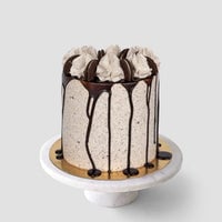 The Last Minute Cakes by Jenna Rae Cakes features a cookies and cream layer cake with chocolate drip, swirls of cookies and cream frosting, and cookie halves, shown on a marble stand against a gray background.