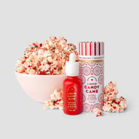 A bowl of popcorn with red and green sprinkles sits beside a striped container and a red bottle of Jenna Rae Cakes Liquid Candy Cane - Package of 6, all on a light gray background.