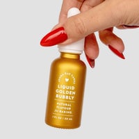 A hand with long red nails holds a small gold bottle of Jenna Rae Cakes Liquid Golden Bubbly - Package of 6, Natural Flavour for Baking, 1 FL OZ / 30 mL, against a plain light background.
