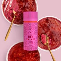 Three bowls of red velvet crème brûlée are topped with caramelized sugar and gold spoons. In the center sits a pink Jenna Rae Cakes Liquid Red Velvet - Package of 6, perfect for baking and drinks.