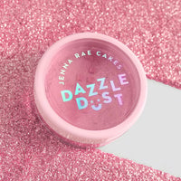 A small pink container labeled Jenna Rae Cakes Lollipop Edible Glitter - 5g Shaker (Package of 6) sits on a sparkling pink glitter surface, with white and iridescent text standing out on the lid.
