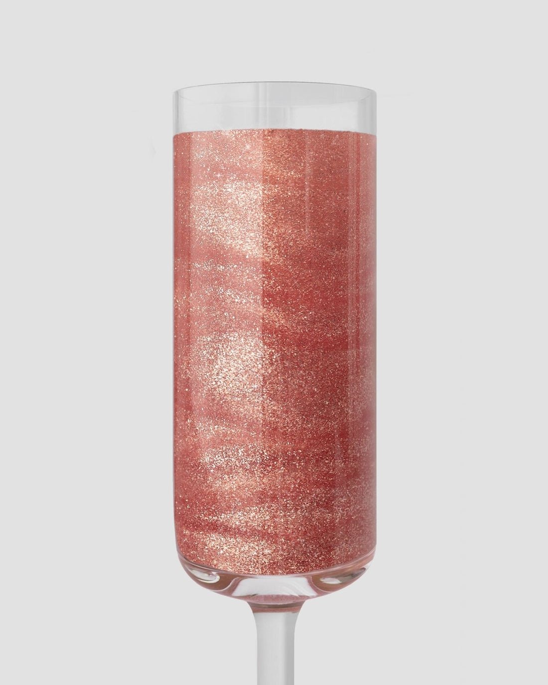 A champagne flute sparkles with a rose-gold drink, shimmering from Jenna Rae Cakes Lucky Penny Edible Glitter—20g containers, package of 3—set against a light gray background.