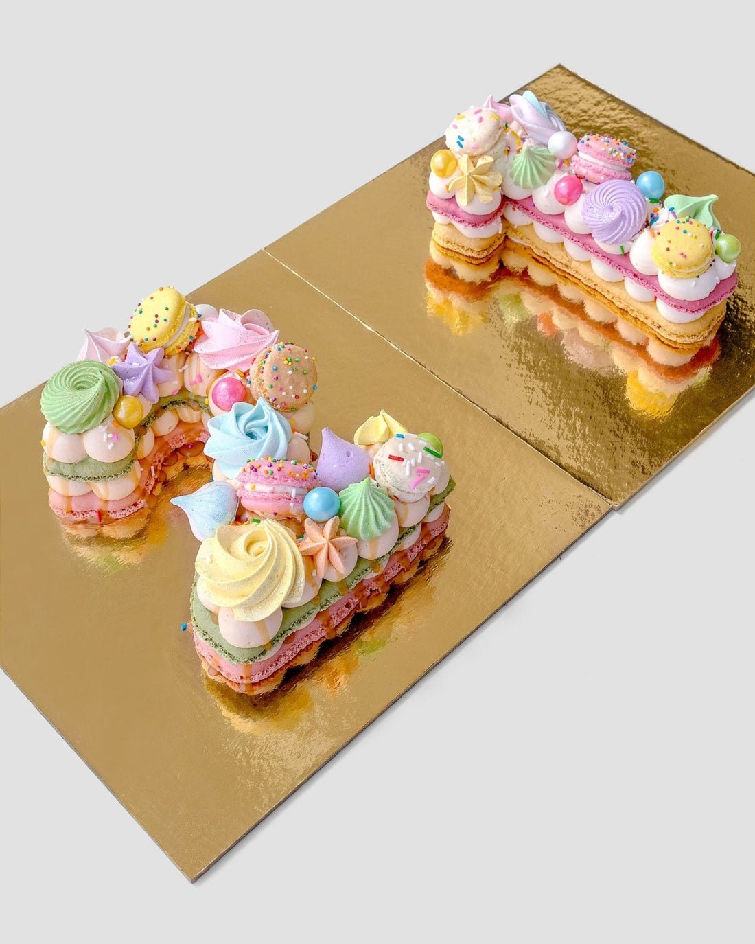 The Jenna Rae Cakes Macaron Number Cake features cakes shaped into the number 21, topped with colorful meringues, macarons, candies, and sprinkles, and elegantly displayed on a gold board.