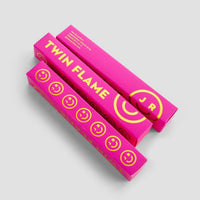Two bright pink rectangular boxes labeled Twin Flame Perfume in bold yellow text, featuring yellow smiley faces and J R in a circle, from Jenna Rae Cakes, displayed on a light gray background.