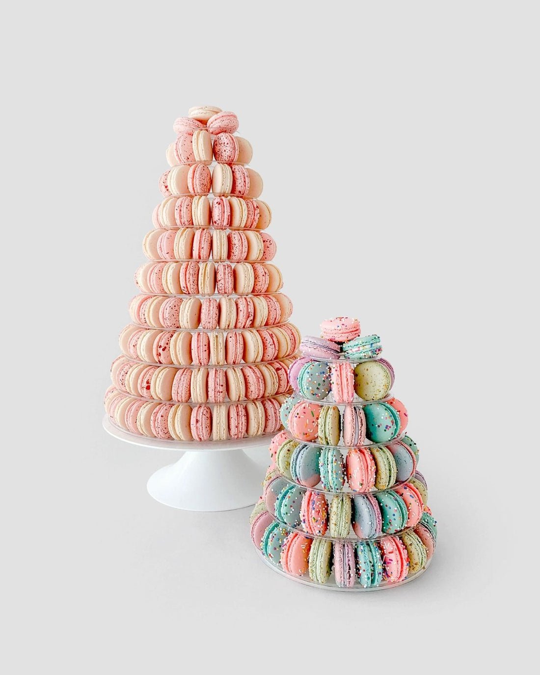 Jenna Rae Cakes’ Dessert Tables feature two cone-shaped macaron towers on white stands: one with pink and cream macarons, the other smaller tower with pastel blue, pink, and purple macarons.