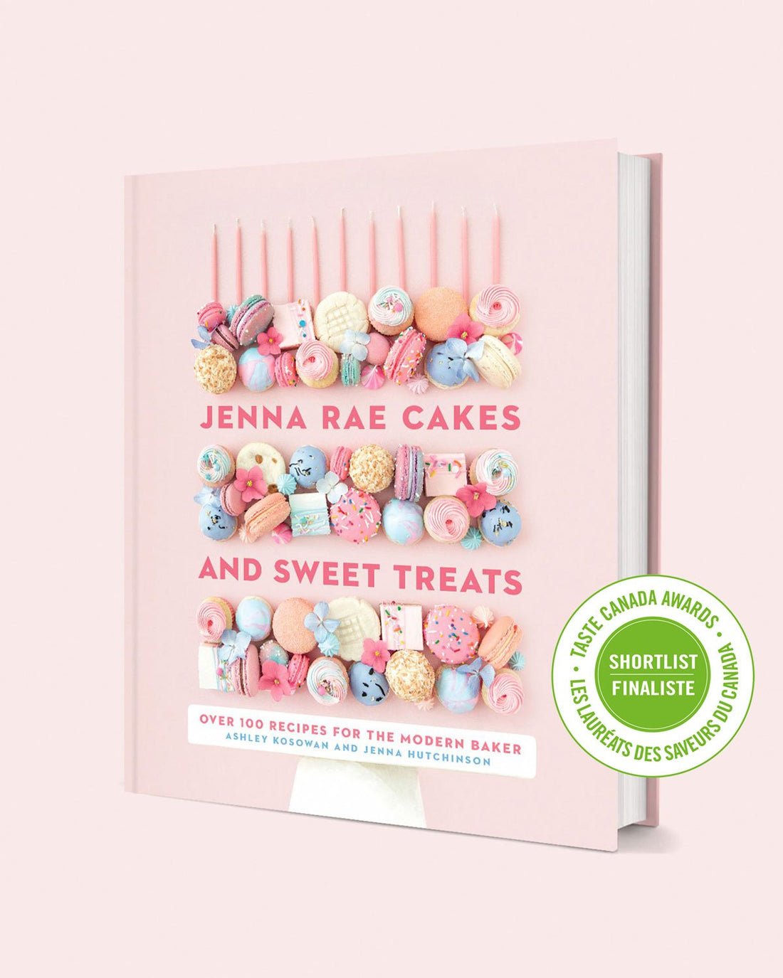 The Jenna Rae Cakes and Sweet Treats Cookbook by Jenna Rae Cakes has a pink cover with colorful desserts like macarons and cupcakes, plus a green sticker showing it’s a Taste Canada Awards shortlist finalist.