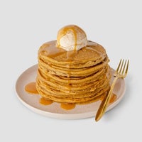 A stack of pancakes topped with Jenna Rae Cakes Liquid Pumpkin Spice and a scoop of ice cream, drizzled with syrup, served on a plate with a gold fork.
