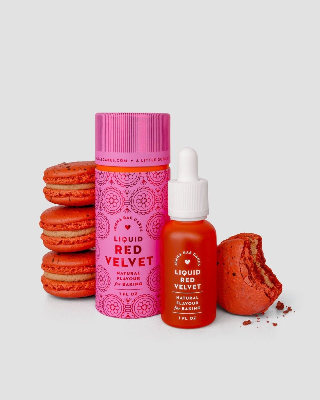 A bottle and container of Jenna Rae Cakes Liquid Red Velvet are shown next to several red macarons—one partially eaten—all set against a simple light gray background.