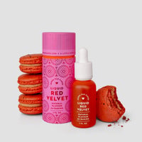A bottle and container of Jenna Rae Cakes Liquid Red Velvet are shown next to several red macarons—one partially eaten—all set against a simple light gray background.