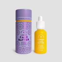 A bottle of Jenna Rae Cakes Liquid Cake Batter with a white dropper cap stands beside its purple cylindrical packaging, both labeled for baking, against a light gray background.