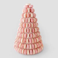 The Macaron Towers by Jenna Rae Cakes feature a tall cone shape with neatly stacked pink and cream macarons arranged in circular tiers, displayed on a light gray background.