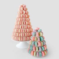 Two Jenna Rae Cakes Macaron Towers are displayed on white stands against a light gray background—one tower features pink macarons, while the other showcases pastel blue, pink, purple, and green macarons.