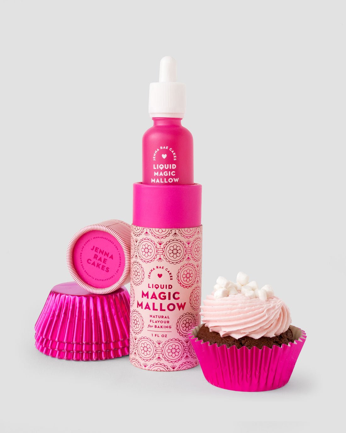 A bright pink Jenna Rae Cakes Liquid Magic Mallow bottle stands next to stacked pink cupcake liners and a chocolate cupcake with pink frosting and mini marshmallows on a light gray background.