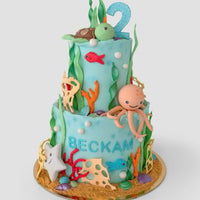 The One-of-a-Kind Cakes by Jenna Rae Cakes features a blue two-tier ocean-themed birthday cake with fondant seaweed, fish, turtle, octopus, starfish, coral, a large number 2 topper, and “Beckam” on the front.