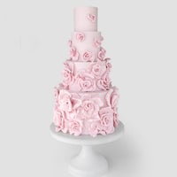 A tall, four-tiered cake decorated with numerous pastel pink fondant roses, displayed on a white pedestal cake stand against a light gray background.