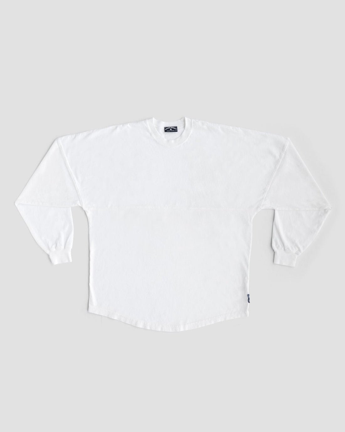 A Jenna Rae Cakes White and Silver Spirit Jersey is laid flat on a light gray background, featuring long sleeves, ribbed cuffs, and a small dark tag on the lower side seam. No visible patterns or logos are present.