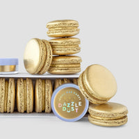 A set of golden macarons is displayed with a Jenna Rae Cakes Antique Gold Edible Lustre Dust (20g, pack of 3) in front, all on a simple light gray background.