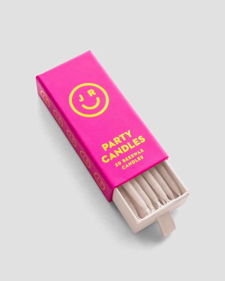 A bright pink Jenna Rae Cakes Party Candles box with a yellow smiley face and 20 beeswax candles displays cream-colored candles, some visible through the open end, set against a light gray background.