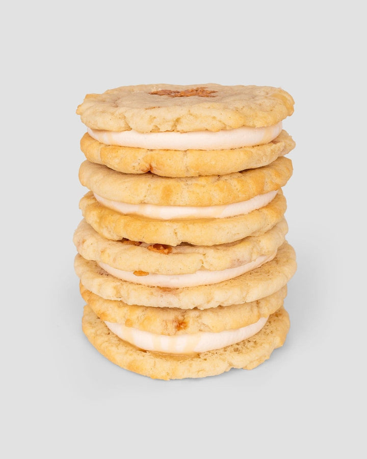 A stack of six Jenna Rae Cakes Regular Cookie Sandwiches, featuring cream filling between two golden cookies, set against a plain light gray background.